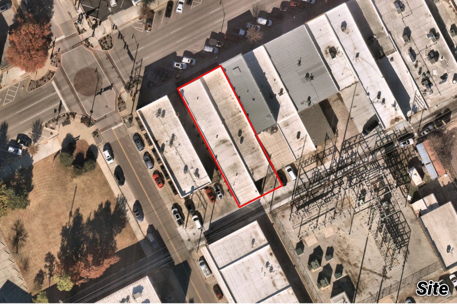 Aerial of the narrow downtown Norman storefront outlined in red among Main Street buildings, near the railroad and an electrical substation.