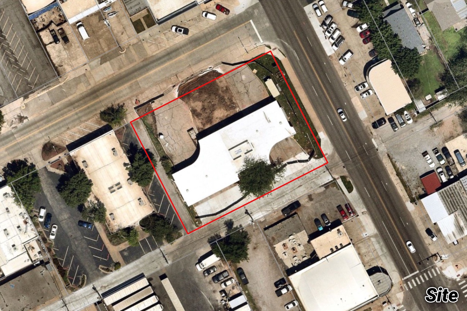 Aerial of the downtown transit-center block outlined in red, with a building and parking near the railroad and surrounding retail.