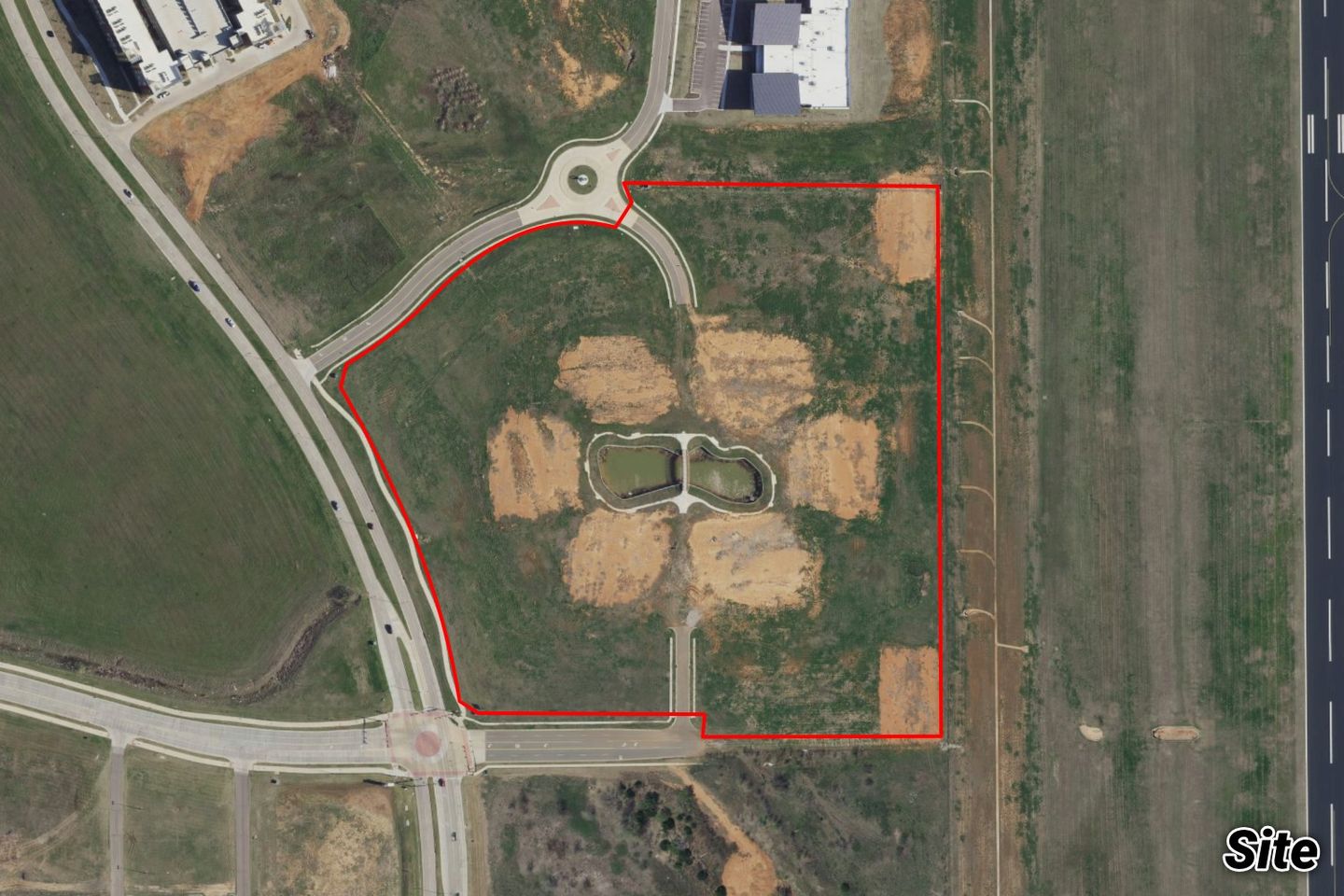 Aerial of the graded MNTC tract outlined in red with a small detention pond, near a roundabout and the airport runway.