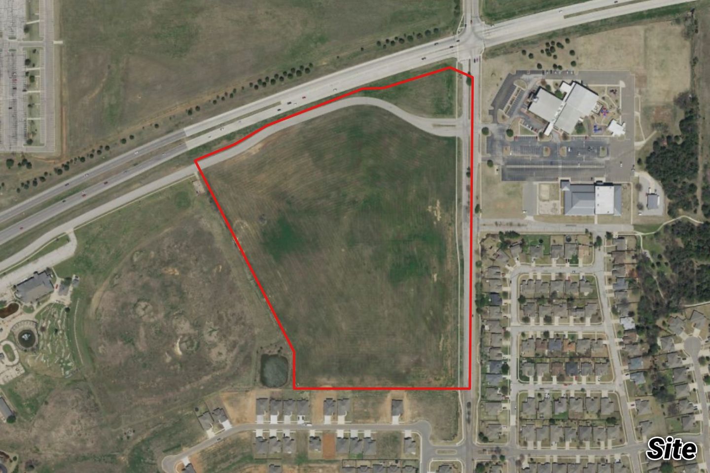 Aerial of the large grassy tract outlined in red along a highway, near a school and a residential neighborhood.