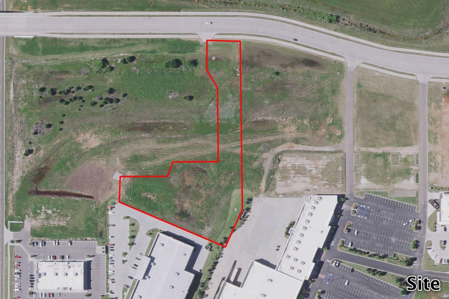 Aerial of the grassy UNP tract outlined in red near existing commercial and industrial buildings along a roadway.