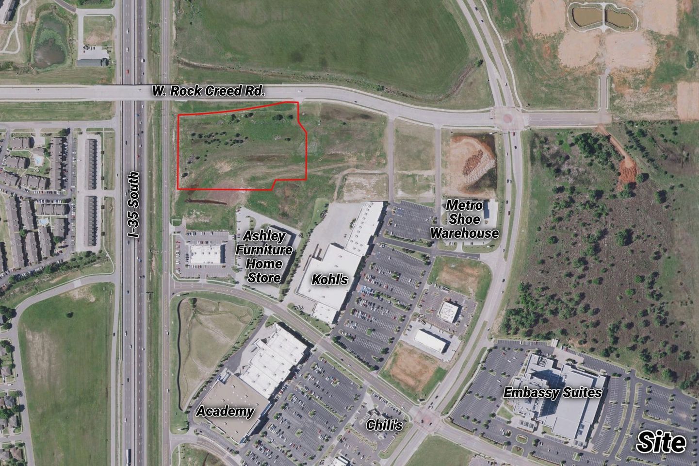 Labeled aerial of the vacant CarMax tract outlined in red on W. Rock Creek Road near Ashley Furniture, Kohl's, Academy, Embassy Suites, and I-35 South.