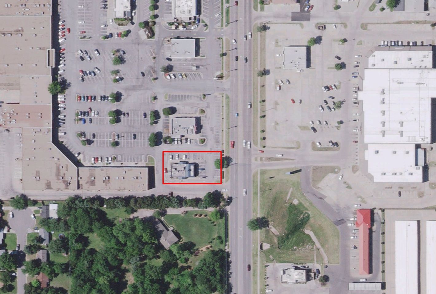 Aerial of the small building-and-parking parcel outlined in red at a commercial intersection, across from a park.